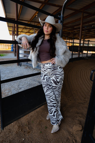 Woman in zebra print pants and cowboy hat standing in a barn.