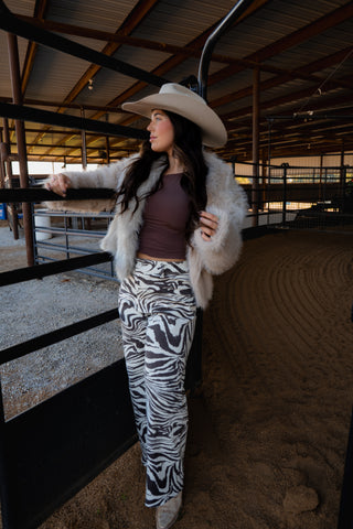 Woman in a fur coat and cowboy hat standing in a barn.