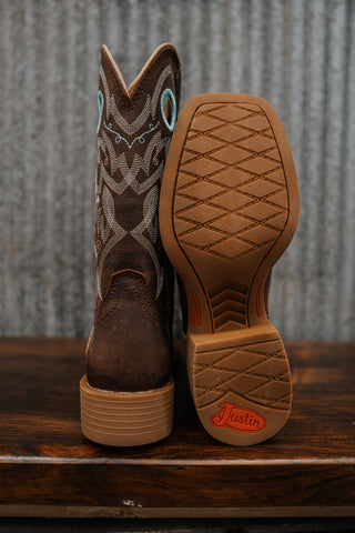 Brown cowboy boot with intricate design on a wooden surface and corrugated metal background