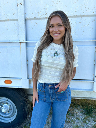 Woman standing in front of a white trailer wearing a white top and blue jeans.