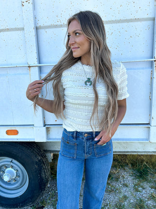 Woman with long blonde hair wearing a white top and blue jeans standing in front of a white trailer.