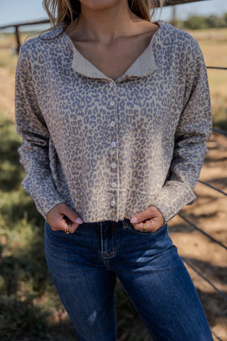 Person wearing a leopard print long-sleeve shirt and blue jeans in an outdoor setting