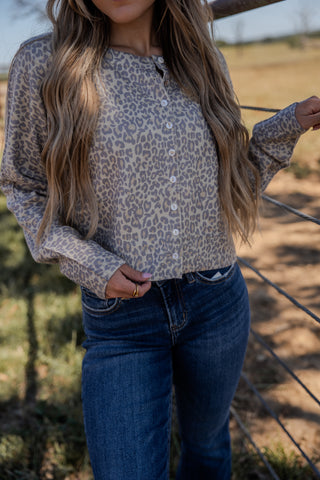 Person wearing a leopard print top and blue jeans standing outdoors.