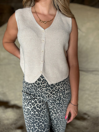 Person wearing a sleeveless button-up top and leopard print pants on a neutral background