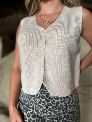 Person wearing a light-colored knitted vest with button details.