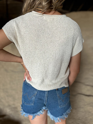 Person wearing a light gray knit top and blue denim shorts with a blurred background