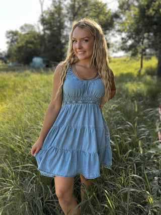 Woman in a blue dress standing in a grassy field with trees in the background
