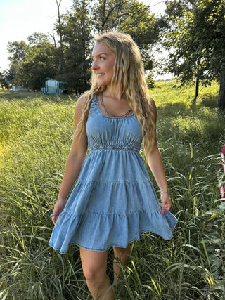 Woman in a blue dress standing in a grassy field with trees in the background