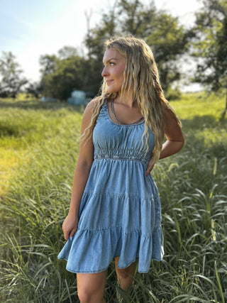 Woman in a blue dress standing in a grassy field with trees in the background