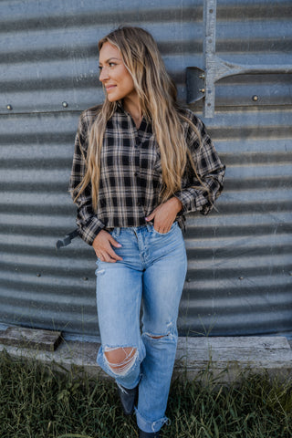 Woman wearing a plaid shirt and jeans standing against a corrugated metal wall.