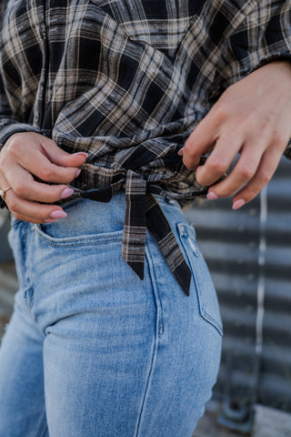 Person wearing a plaid shirt tied around the waist with blue jeans, blurred background