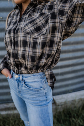 Person wearing a plaid shirt and jeans standing against a corrugated metal wall.