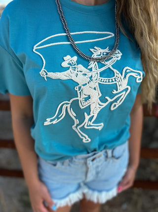 Person wearing a turquoise t-shirt with a white graphic design of a cowboy on a horse.