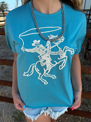 Person wearing a turquoise t-shirt with a graphic design of a cowboy on a horse.