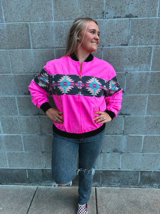 Person wearing a bright pink jacket with patterned sleeves against a gray brick wall.
