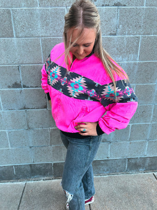 Person wearing a bright pink jacket with a patterned design against a gray brick wall.