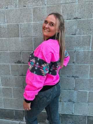 Person wearing a bright pink jacket with floral patterns against a gray brick wall.