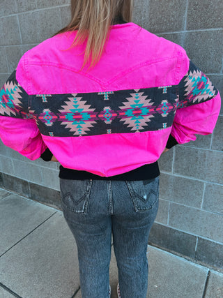 Person wearing a bright pink jacket with a patterned back against a gray wall.