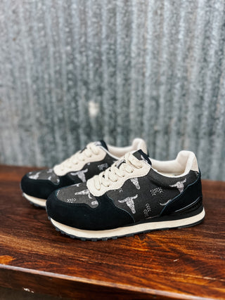Black sneakers with white soles on a wooden surface against a textured gray wall.
