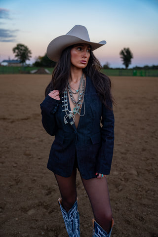 Woman in cowboy hat and blazer standing in an open field at sunset
