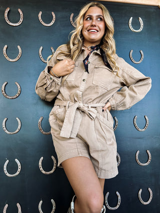 Woman in beige jumpsuit posing against a blue background with horseshoe patterns