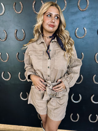 Woman in beige outfit standing against a dark wall with horseshoe patterns