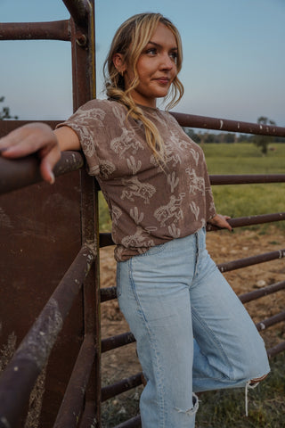 Woman leaning against a rusted metal gate in an open field