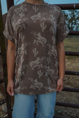 Person wearing a brown t-shirt with white patterns in an outdoor setting