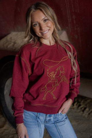 Woman wearing a red sweatshirt with a horse graphic in a rustic setting