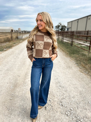 Woman wearing a patterned sweater and jeans standing on a gravel road.