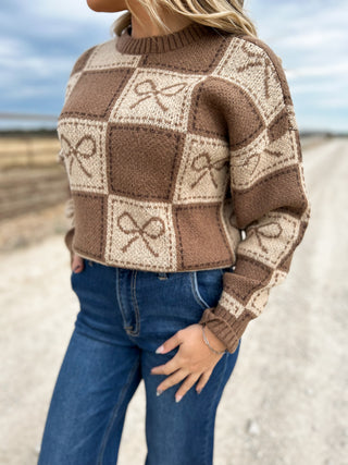 Person wearing a brown and beige checkered sweater with abstract patterns outdoors.