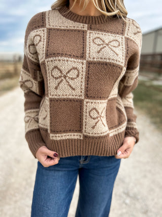 Brown checkered sweater with abstract patterns worn by a person outdoors.