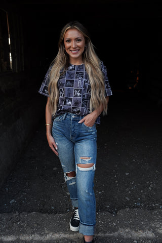 Woman wearing a patterned shirt and ripped jeans standing in a dark alleyway.