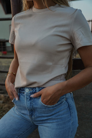 Person wearing a beige t-shirt and blue jeans with a blurred background
