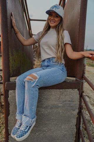 Woman sitting on a metal structure wearing a cap, t-shirt, and jeans.