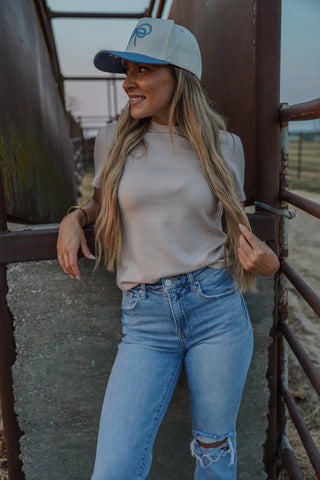 Woman wearing a cap and casual outfit leaning against a metal railing.