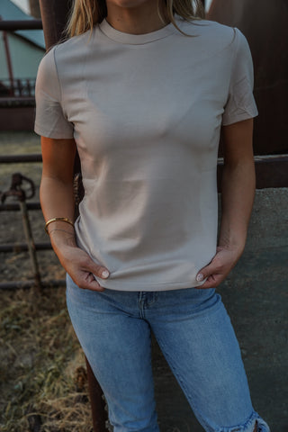 Person wearing a plain beige t-shirt and blue jeans outdoors.