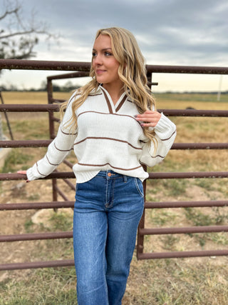 Woman wearing a striped sweater and jeans standing in front of a metal gate.