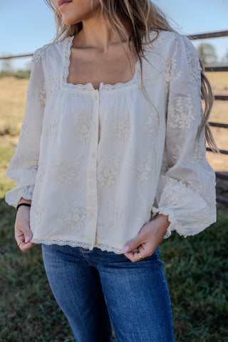 Woman wearing a white lace blouse and blue jeans outdoors.