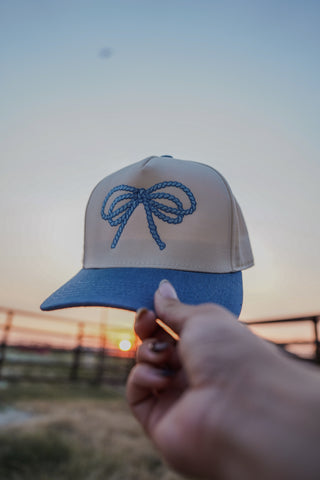 Cap with a blue bow design held against a sunset sky