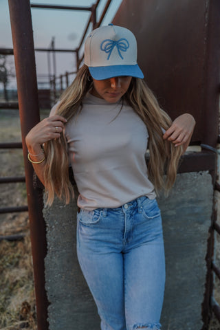 Woman wearing a cap and jeans standing against a rustic metal gate.