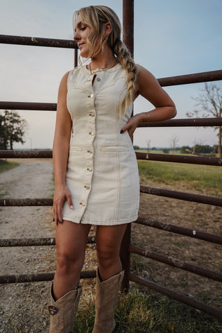 Woman in a white dress with buttons standing next to a metal fence outdoors.