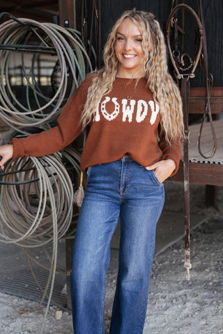 Woman wearing a brown sweater with 'LOWDY' text and blue jeans, standing in front of coiled ropes.