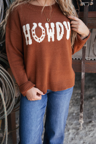 Person wearing a brown sweater with 'HOWDY' printed on it, standing in an indoor setting.