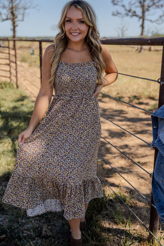 Woman in a floral dress standing in a field with a fence in the background