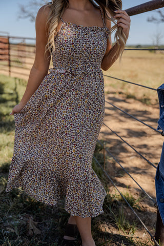 Woman wearing a floral dress standing near a fence with a field in the background