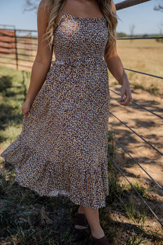 Woman wearing a floral dress standing in a field with a fence in the background