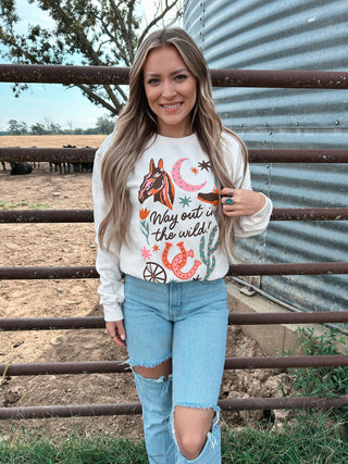 Woman wearing a white sweatshirt with a horse graphic and text, standing in front of a metal fence and silo.