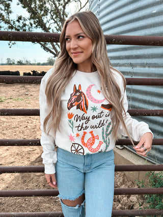 Woman wearing a sweatshirt with horse graphics and text, standing in front of a metal fence and field.