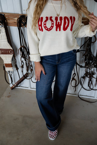 Person wearing a cream sweatshirt with 'HOWDY' in red text, standing in a stable.